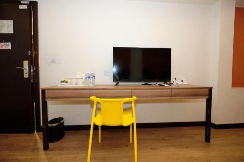a yellow chair in front of a desk with a television at Memoire Hornbill Hotel Kuching Sarawak in Kuching