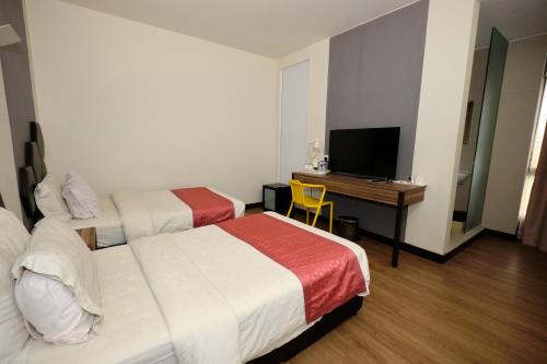 a hotel room with two beds and a desk with a television at Memoire Hornbill Hotel Kuching Sarawak in Kuching