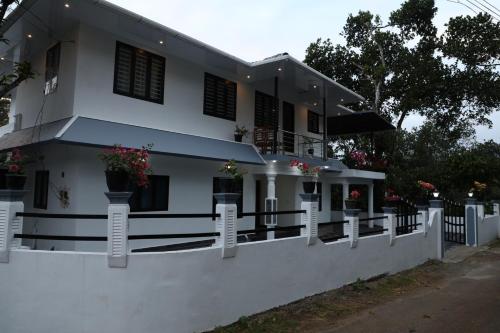 a white house with a fence in front of it at Bougainvillea Homestay in Nedukandam