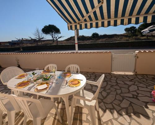 une table et des chaises blanches sur une terrasse avec un parasol dans l'établissement Sol-y-Days Altitude Zéro en première ligne face à la plage, au Grau-du-Roi