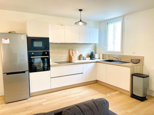 une cuisine avec des armoires blanches et un réfrigérateur en acier inoxydable dans l'établissement La Suite Côté Loire, à Orléans