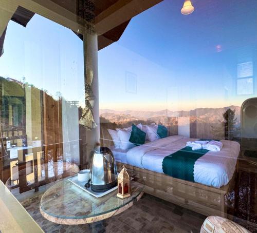 a bedroom with a large window with a bed and a table at The Sky Mountain Kufri I Serviced Villa I Balcony I Valley and Mountain View I Family Groups & Bonfire I Memories & Enjoyment Villa I Operated Charvi Retreat by Exotic Stays in Kūfrī