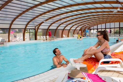 un homme et une femme assis dans une piscine dans l'établissement Mobil home Céleste 6-8 personnes, à Litteau