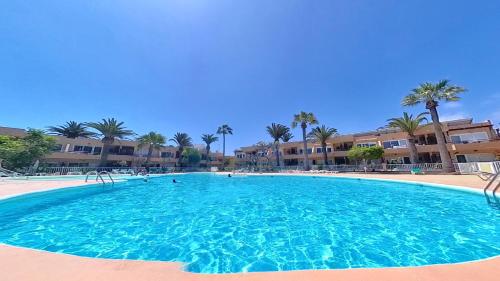 a large blue swimming pool with palm trees and buildings at Residencial Las Dunas, Best Holiday Home Resort On The Island- VV in Corralejo