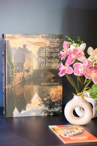 a book and a vase with flowers on a table at Gillis Eight Guest Rooms by Romy&Travis in Bruges