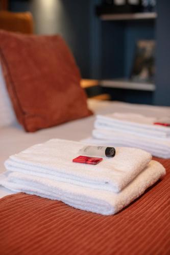 a stack of white towels on a bed with a remote control at Gillis Eight Guest Rooms by Romy&Travis in Bruges