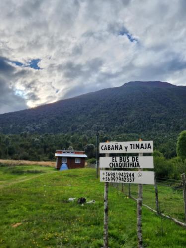 a sign in a field with a mountain in the background at Cabañas y tinaja El bus de chaqueihua in Hornopiren