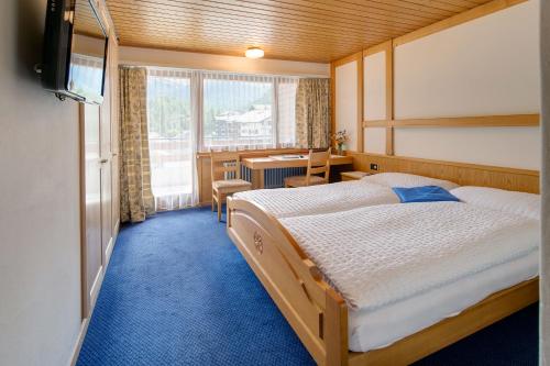 a bedroom with two beds and a desk and a television at Hotel Parnass in Zermatt