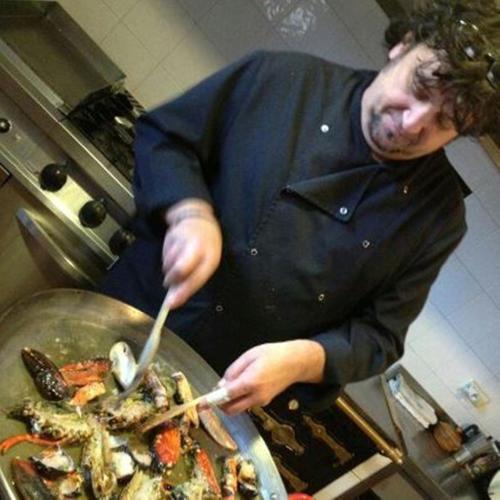 a man in a kitchen preparing food in a wok at El Quesar de Gamoneo in Gamonedo de Cangas