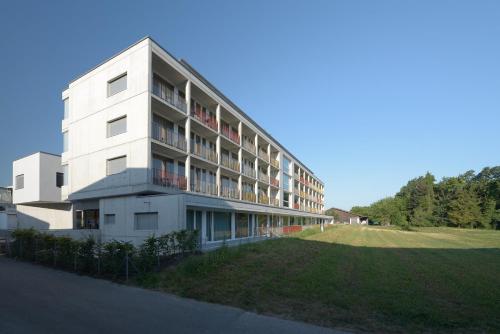 a white building with a grassy field in front of it at Hotel Frauenfeld in Frauenfeld