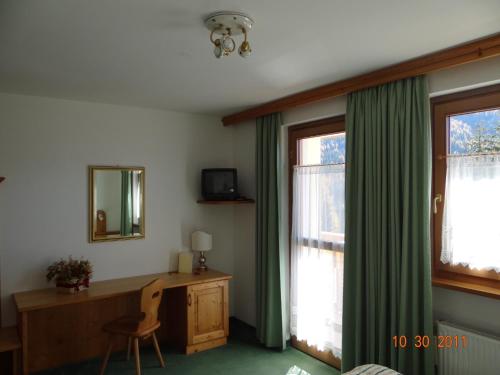 a room with a desk and a window with green curtains at Hotel Mondeval in Selva di Cadore