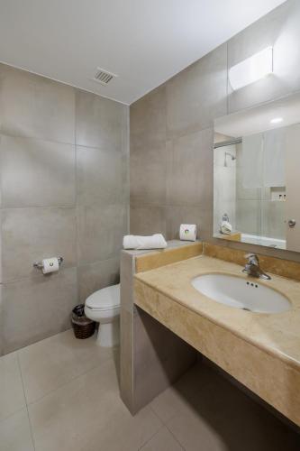 a bathroom with a sink and a toilet and a mirror at Hotel Suites México Plaza León Campestre in León