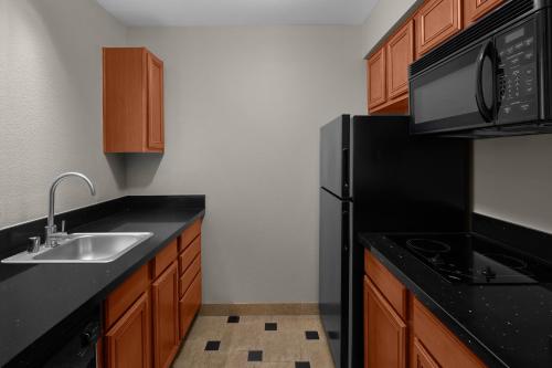 a kitchen with a sink and a black refrigerator at Larkspur Landing Extended Stay Suites Roseville in Roseville