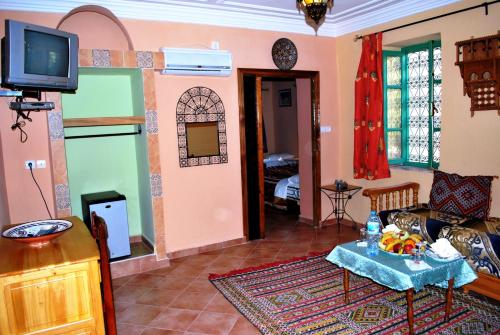 a living room with a table and a tv in it at Riad Mimouna De Timnay in Aguelmous