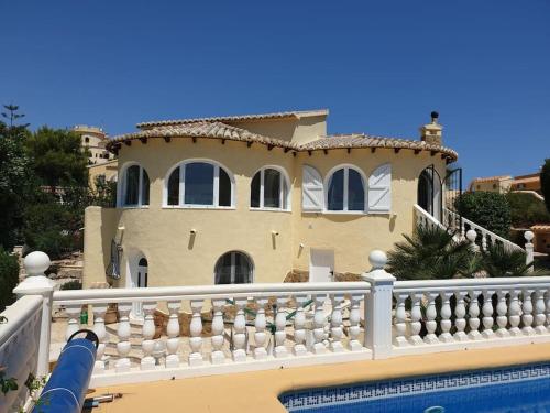 a house with a white fence next to a swimming pool at "Traumhaftes Ferienhaus mit Pool und Meerblick - Cumbre del Sol erleben!" in Benitachell