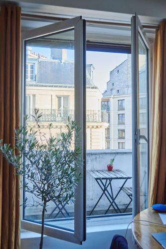 Une porte ouverte s'ouvre sur un balcon avec une table et un arbre. dans l'établissement Studio cosy avec balcon Paris 16ème, à Paris