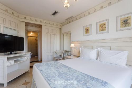 a bedroom with a white bed and a flat screen tv at Studios frente ao mar no IL Campanario Resort ILCTOP in Florianópolis