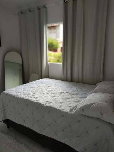 a bedroom with a white bed with a window at Casa aconchegante no centro da cidade in São Thomé das Letras