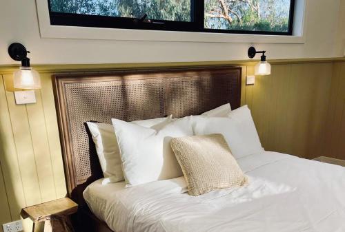 a bed with white pillows and a television above it at Phillip Island Coastal Cabins in Sunderland Bay