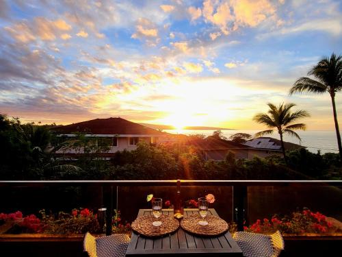 a table and chairs on a balcony with the sunset at Hale Mai Hopohopo in Kahana