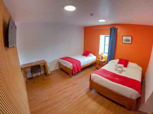 2 Betten in einem Zimmer mit orangefarbenen Wänden und Holzböden in der Unterkunft Hotel Casa Campesina in Cusco
