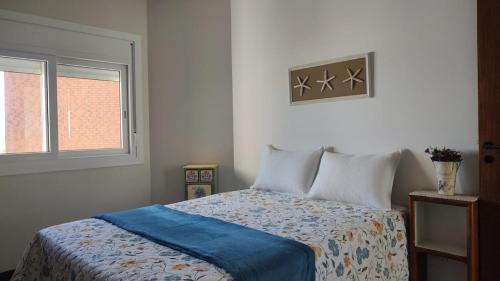Un dormitorio con una cama con una manta azul y una ventana. en Apto Torres com vista para o Mar, 3 suítes, sacada com churrasqueira, en Torres