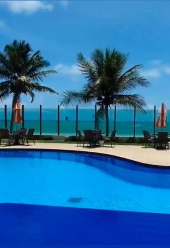 a swimming pool with palm trees and the ocean at Cobertura Duplex Pé na Areia 509 Tabatinga Residence in Conde