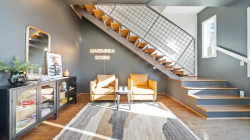a living room with a staircase with two chairs and a table at Chic Modern Condo in the Vibrant NuLu District in Louisville