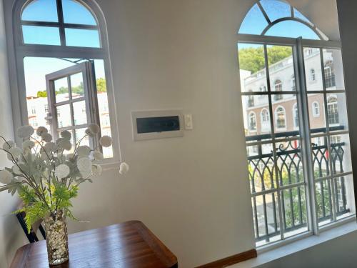 a vase of flowers on a table in front of two windows at Sun'House- Family 2BR Apt View Sea & Sunset Town Phu Quoc in Phu Quoc