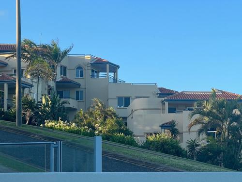 a white building with palm trees and a fence at Villa Mar Colina in Yeppoon