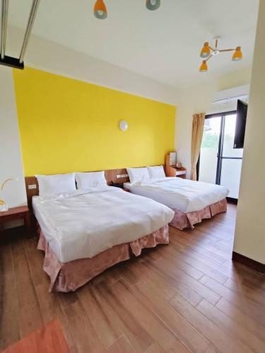 two beds in a room with a yellow wall at 海葵民宿-全新獨棟 in Chenggong