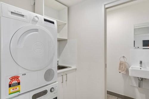 a white laundry room with a washer and a sink at Crown Beach Escape - Stylish Comfort by the Sea in Wollongong