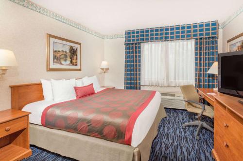 a hotel room with a bed and a desk and a television at Ramada by Wyndham Kent Seattle Area in Kent
