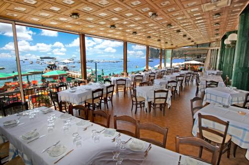 een restaurant met witte tafels en stoelen en de oceaan bij Hotel La Certosa in Massa Lubrense