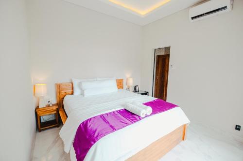 a bedroom with a large white bed with purple sheets at Turtle Shelter Guest House in Sanur