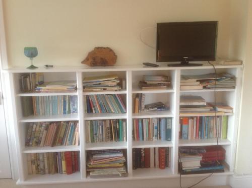 a white book shelf filled with books and a tv at The Coach House in Ross on Wye