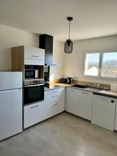 une cuisine avec des armoires blanches et un four à plaques de cuisson dans l'établissement Maison du Cos, neuve avec 3 chambres et un garage, à Lamothe-Capdeville