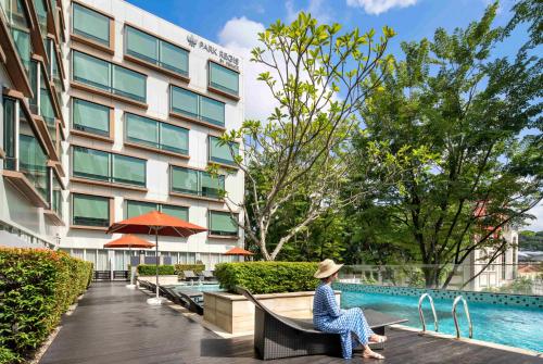 a woman sitting on a bench in front of a building at Park Regis by Prince Singapore - Newly Renovated in Singapore