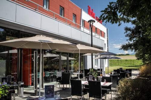 a restaurant with tables and umbrellas in front of a building at Ibis Saint-Genis-Pouilly Genève in Saint-Genis-Pouilly