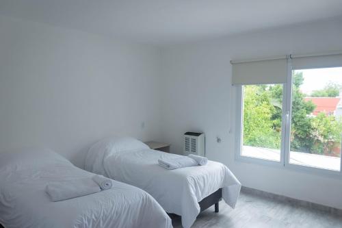 two beds in a white room with a window at Bahia Urban Apartments in Bahía Blanca