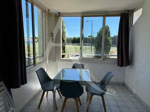 une table et des chaises en verre dans une pièce avec fenêtres dans l'établissement LA PLAGE AU BOUT DE LA RUE, à Sète