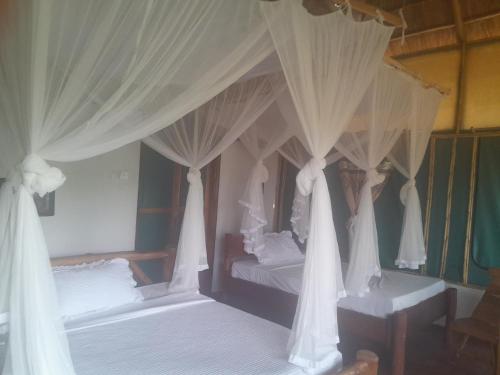 a bedroom with two beds with white drapes at Entale Safari Camp Queen Elizabeth National Park in Kasese