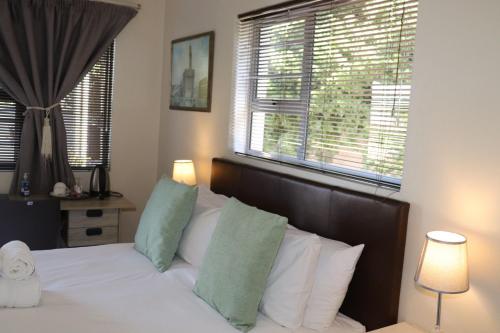 a bedroom with a bed with white pillows and two windows at Tygerviews on Uys in Tygerberg Hills