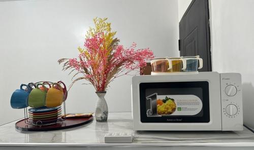 un micro-ondes posé sur une table avec un vase de fleurs dans l'établissement HOMEY STAYCATION WITH PARKING near Diliman, Katipunan, Commonwealth, à Manille
