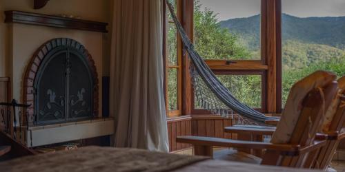 a bedroom with a fireplace and rocking chairs in front of a window at Mirante da Colyna Hotel & SPA in Monte Verde