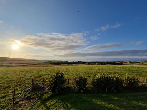 a field of grass with the sun in the sky at Borlum House in Thurso