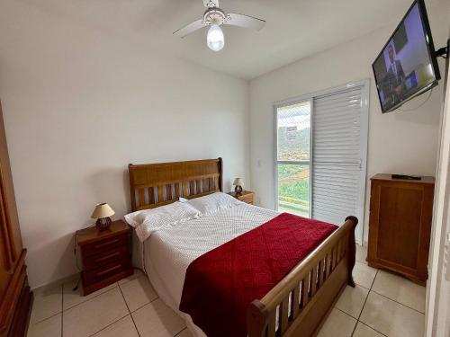 Un dormitorio con una cama con una manta roja y una ventana. en Edifício Baalbek, en Mongaguá