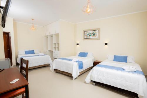 a bedroom with two beds and a table and a desk at Hotel San Marino Tarapoto in Tarapoto