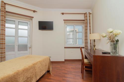 a bedroom with a bed and a desk with a vase of flowers at Hospedaria Maioral in Vila Franca de Xira