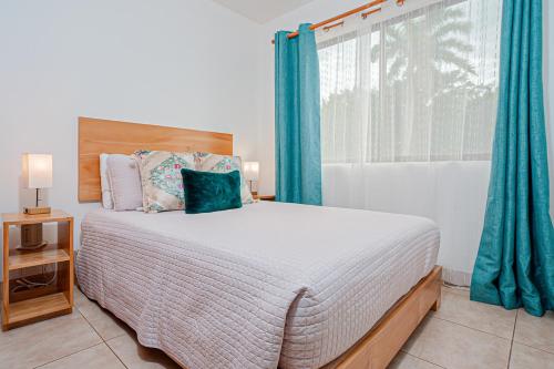 a bedroom with a bed with blue curtains and a window at Palmas de Tamarindo 201D in Tamarindo